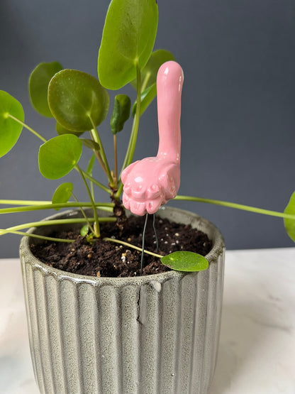 Pink flamingo in a pot with green leaves against a gray background